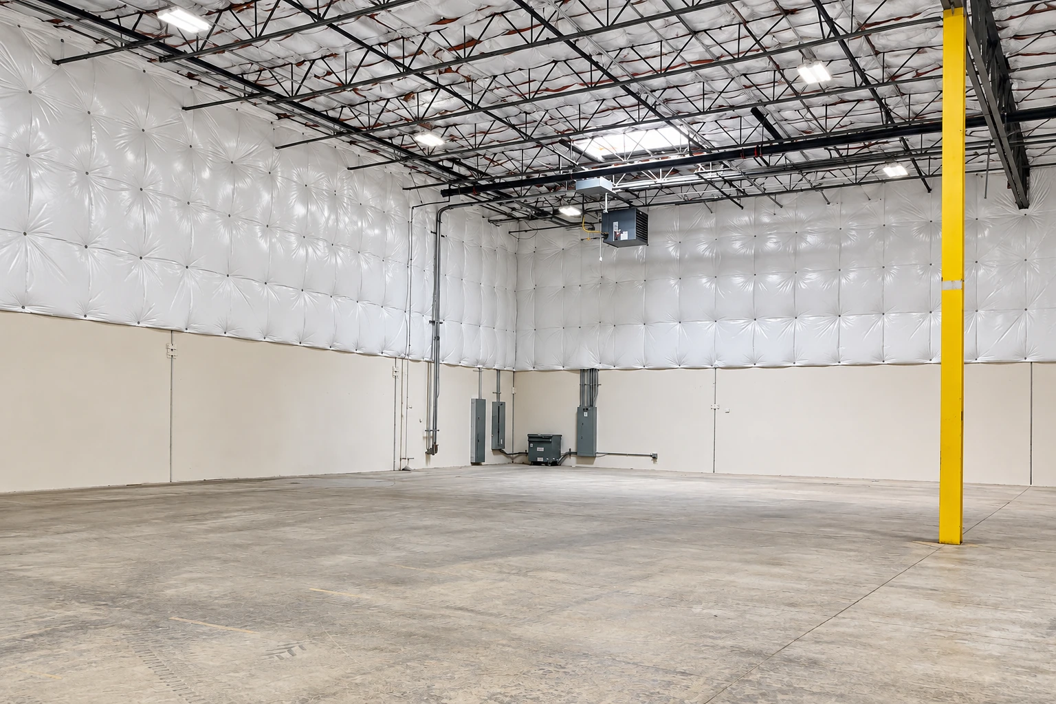 Commercial warehouse interior with white insulation lining the upper walls and roof, exposed steel trusses, and a yellow support column.