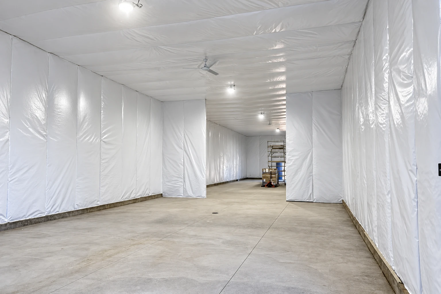 A long commercial interior has white insulation covering its walls and ceiling above a bare concrete floor.