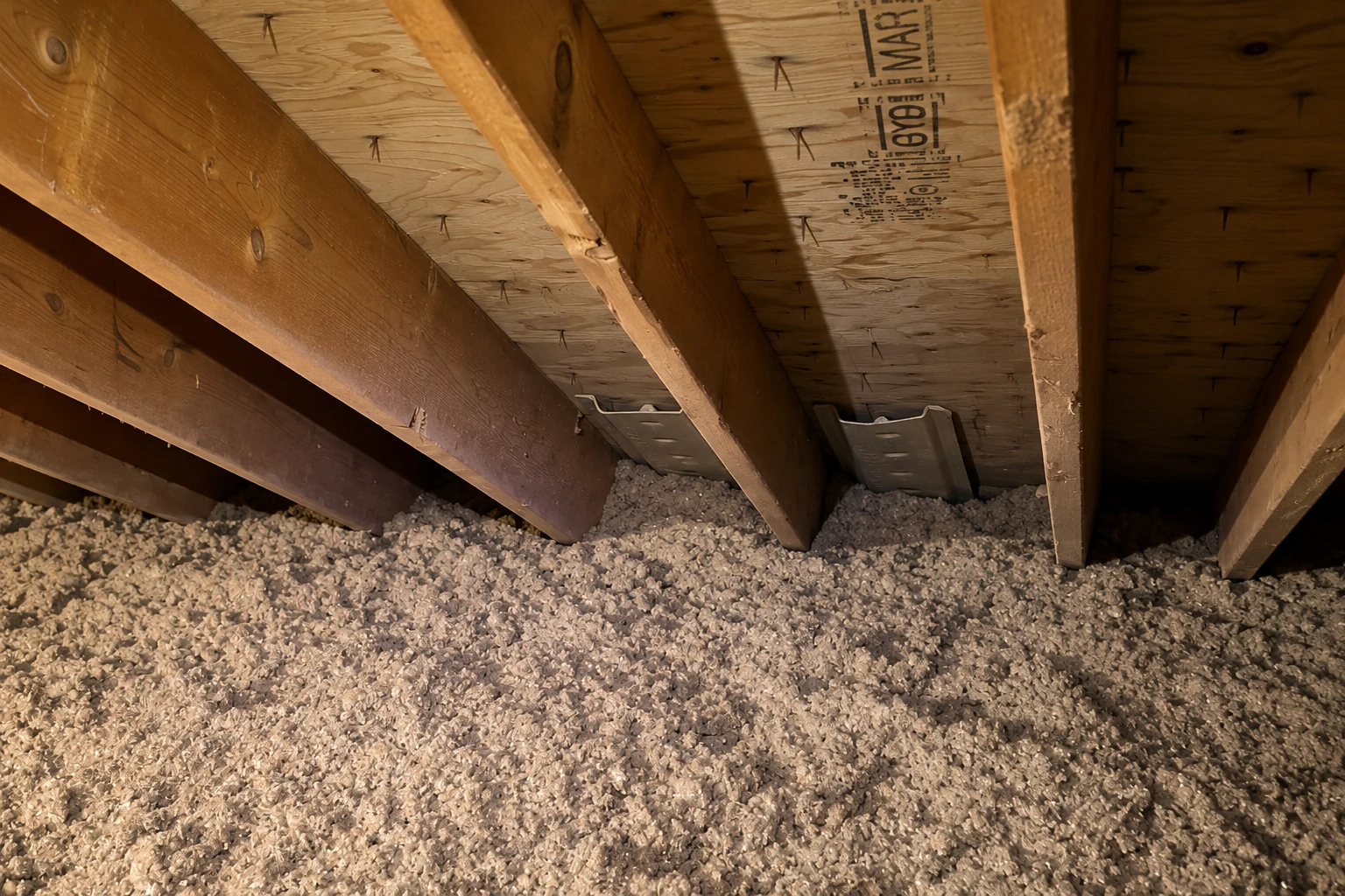 Loose-fill insulation is spread across an attic floor between exposed wooden joists.